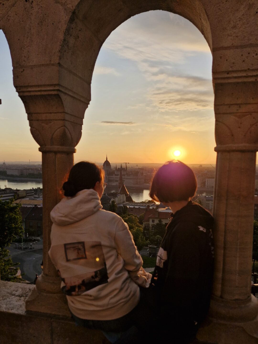 Auf dem Bild sieht man zwei Frauen, welche den Sonnenaufgang beobachten. Sie sitzen in einem Fensterbogen.