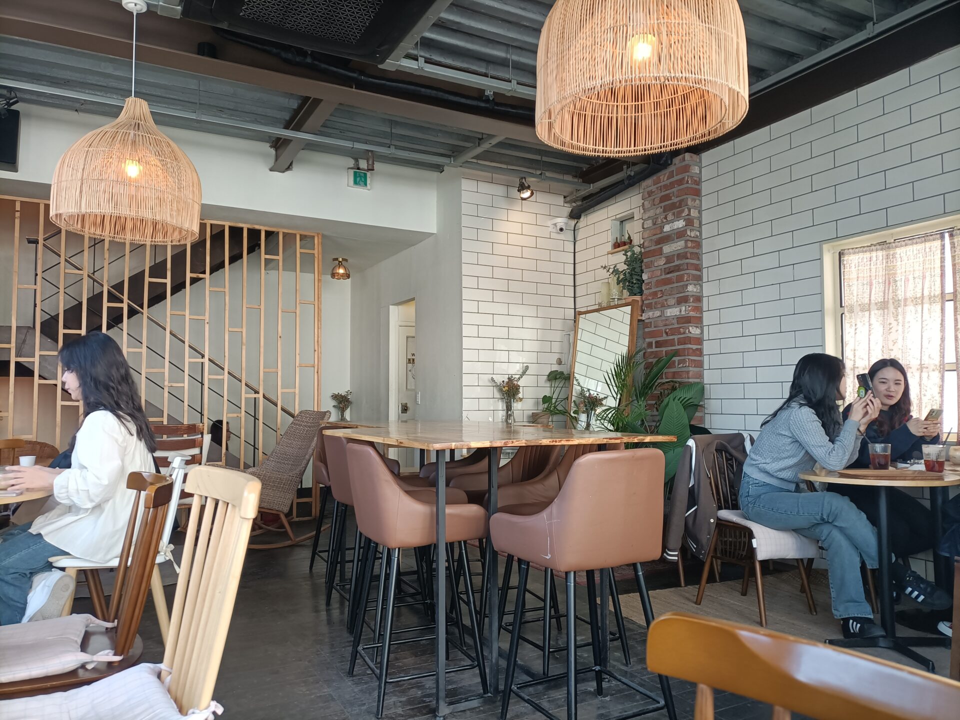 Ein Café mit einigen Tischen und Stühlen. Zwei Lampen hängen von der Decke. Ein paar Leute unterhalten sich.