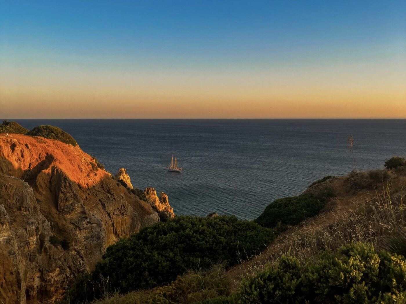 Saudade: The Feeling I Carried Home from Portugal 1 IMG 9124 View of the sea with a sailboat sailing on it at sunset from the cliffs on the coast in Lagos (Algarve).
